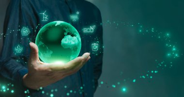 Bir el, çevresel sürdürülebilirliği sembolize eden, geri dönüşüm, güneş enerjisi ve rüzgar enerjisi gibi çevre dostu sembollerle çevrili, parlayan yeşil bir gezegen tutuyor..
