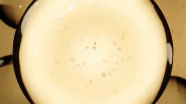 Yumuşak bir kehribar zemin üzerinde yüzen yarı saydam altın sıvı baloncuklar yakın plan, sakin ve soyut bir kompozisyon oluşturur.