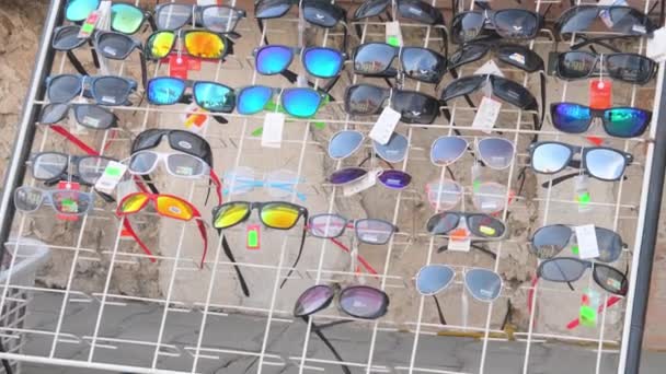 小さな雑貨店の前にサングラス付きのディスプレイラック 様々なサングラス付きの小売ラック ヨーロッパの通り — ストック動画