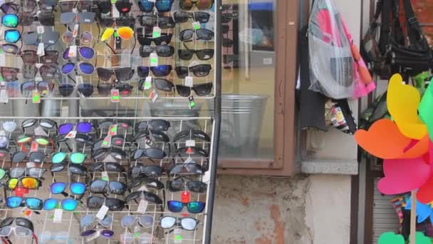 在一家普通小商店前展示带太阳镜的架子 在一家商店前面有各种太阳镜的零售架 在一家普通小商店前面放有人造花的盒子 — 图库视频影像