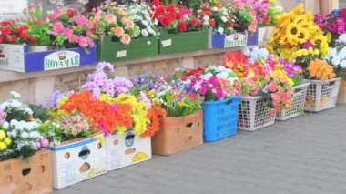 Küçük bir marketin önündeki yapay çiçeklerle dolu kutular. Varyete mağazasının önünde yapay plastik çiçeklerin perakende satışı. Avrupa 'daki cadde.