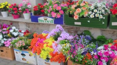 Küçük bir marketin önündeki yapay çiçeklerle dolu kutular. Varyete mağazasının önünde yapay plastik çiçeklerin perakende satışı. Avrupa 'daki cadde