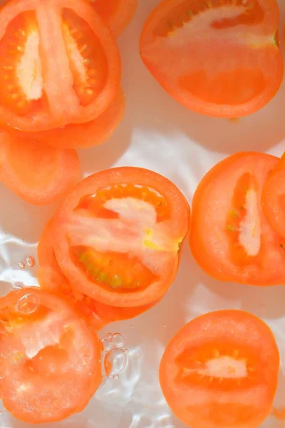 Close-up fresh slices of juicy tomato on white background. Slices of tomato in sparkling water on white background, closeup. Vertical image.