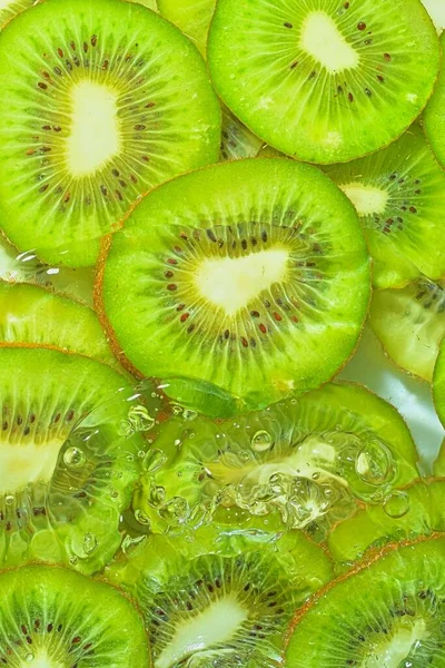 Close-up fresh slices of juicy kiwi fruit on white background. Slices of kiwi fruit in sparkling water on white background, closeup. Vertical image.