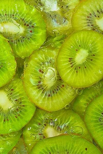 Close-up fresh slices of juicy kiwi fruit on white background. Slices of kiwi fruit in sparkling water on white background, closeup. Vertical image.