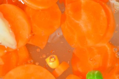 Taze sebzeli kaynar su, yakın plan. Sebzelerin havuç, bezelye, karnabahar ve su arka planında mısırla yakın plan görüntüsü. Makro kabarcıklı haşlanmış sebze dokusu.