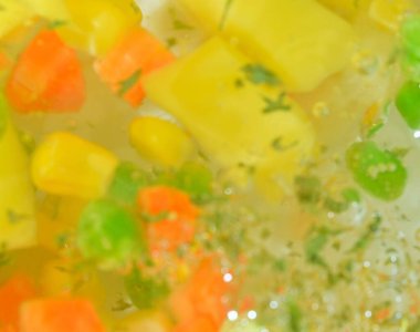 Taze sebzeli kaynar su, yakın plan. Havuçlu, bezelyeli, karnabaharatlı, mısırlı, doğranmış patatesli ve maydanozlu çorba sebzelerinin yakından görüntüsü. Kaynama dokusu