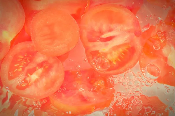 Slices of tomato in water on white background. Tomato close-up in liquid with bubbles. Slices of red ripe tomato in water. Macro image of vegetable in water.