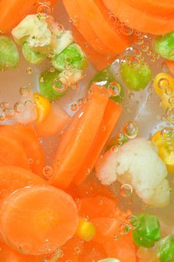 Taze sebzeli kaynar su, yakın plan. Sebzelerin havuç, bezelye, karnabahar ve su arka planında mısırla yakın plan görüntüsü. Makro kabarcıklı haşlanmış sebze dokusu.