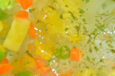 Taze sebzeli kaynar su, yakın plan. Havuçlu, bezelyeli, karnabaharatlı, mısırlı, doğranmış patatesli ve maydanozlu çorba sebzelerinin yakından görüntüsü. Kaynama dokusu