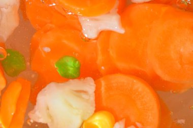 Taze sebzeli kaynar su, yakın plan. Sebzelerin havuç, bezelye, karnabahar ve su arka planında mısırla yakın plan görüntüsü. Makro kabarcıklı haşlanmış sebze dokusu.