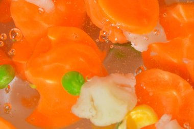 Sebzelerin yakın plan görüntüsü, havuç, bezelye, karnabahar ve su arka planında mısır. Haşlanmış sebze çorbası. Düz tasarım, üst manzara. Yatay makro görüntü. Odaklanmamış.