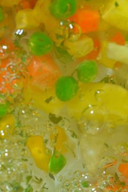 Taze sebzeli kaynar su, yakın plan. Havuçlu, bezelyeli, karnabaharatlı, mısırlı, doğranmış patatesli ve maydanozlu çorba sebzelerinin yakından görüntüsü. Kaynama dokusu