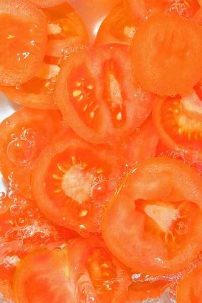Close-up fresh slices of juicy tomato on white background. Slices of tomato in sparkling water on white background, closeup. Vertical image.