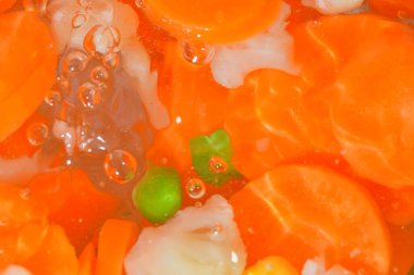 Sebzelerin yakın plan görüntüsü, havuç, bezelye, karnabahar ve su arka planında mısır. Kaynayan çorba veterinerlerinin dokuları makro baloncuklu içerler. Düz tasarım, üst manzara. Yatay resim