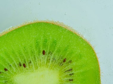 Köpüklü taze kivi ve meyve dilimi. Soda içindeki kivi meyveli dilimin yakın çekimi. Kivi meyveli baloncuklar. Karbonatlı suda bir dilim kivi meyvesi. Makro resim.