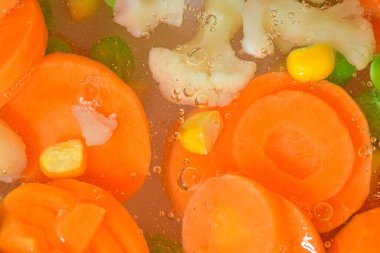 Taze sebzeli kaynar su, yakın plan. Sebzelerin havuç, bezelye, karnabahar ve su arka planında mısırla yakın plan görüntüsü. Cam duvarında makro kabarcıklar olan haşlanmış sebzelerin dokusu. Düz tasarım, üst manzara. Yatay i