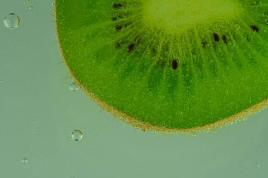 Baloncuklu kivi meyvesinin yakın plan çekimi. Yeşil olgun kivi meyvesini köpüklü suyla dilimleyin. Karbonatlı suda sulu kivi meyvesi. Makro resim.