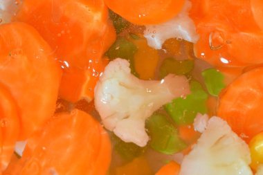 Close-up fresh soup vegetables with carrots, peas, cauliflower and corn on white background. Soup vegetables with carrots, peas, cauliflower and corn in boiling water on white background, close-up. Horizontal image. Top view, flat design. Defocused.