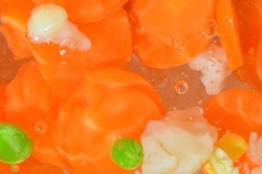 Close-up fresh soup vegetables with carrots, peas, cauliflower and corn on white background. Soup vegetables with carrots, peas, cauliflower and corn in boiling water on white background, close-up. Horizontal image. Top view, flat design. Defocused.