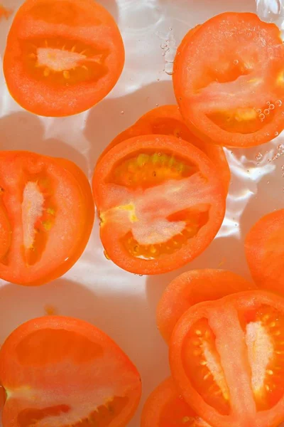 Close-up fresh slices of tomato on white background. Slices of tomato in sparkling water on white background, close-up. Vertical image.