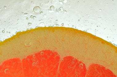 Close-up of a grapefruit slice in liquid with bubbles. Slice of red ripe grapefruit in water. Close-up of fresh grapefruit slice of red o on white background.