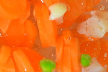 Close-up fresh soup vegetables with carrots, peas, cauliflower and corn on white background. Soup vegetables with carrots, peas, cauliflower and corn in boiling water on white background, close-up. Horizontal image. Top view, flat design. Defocused.