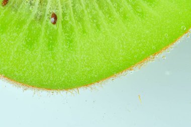 Arka planda taze kivi dilimi yakın plan. Açık arkaplanda köpüklü suyla olgun yeşil kivi meyvesi dilimi. Soda içinde kivi meyvesi yakın çekim. Yatay resim.
