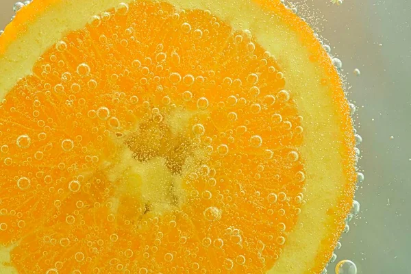 Slice of orange in sparkling water. Orange fruit slice covered by bubbles in carbonated water. Orange slice in water with bubbles.