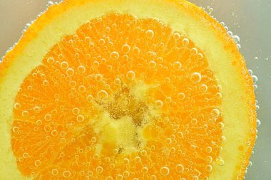 Close-up of an orange slice in liquid with bubbles. Slice of ripe orange fruit in water. Close-up of fresh orange slice covered by bubbles.