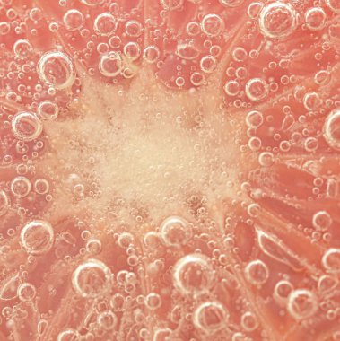 Slice of grapefruit in sparkling water. Grapefruit slice covered by bubbles in carbonated water. Grapefruit slice in water with bubbles.