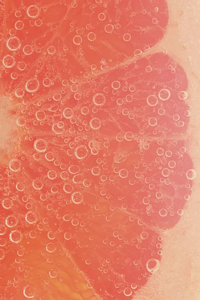 Slice of grapefruit in sparkling water. Grapefruit slice covered by bubbles in carbonated water. Grapefruit slice in water with bubbles.