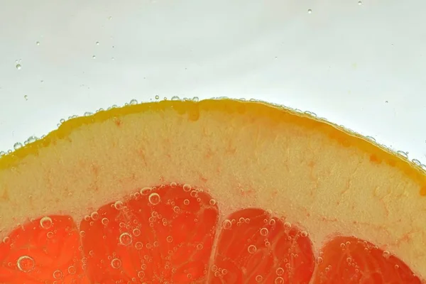 Slice of red grapefruit in water on white background. Grapefruit close-up in liquid with bubbles. Slice of red ripe grapefruit in water. Macro image of fruit in water.