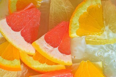 Close-up view of the grapefruit, orange fruit and honey pomelo slices in water background. Texture of cooling fruit drink with macro bubbles on the glass wall. Flat design. Horizontal macro image. Summer fruit background.