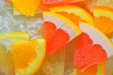 Fresh slices of grapefruit, orange fruit and honey pomelo on white background. Pieces of grapefruit, orange fruit and honey pomelo in sparkling water on white background, close-up. Horizontal macro image. Top view, flat design. Summer fruit backgroun