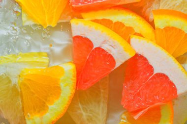 Pieces of grapefruit, orange fruit and honey pomelo in liquid with bubbles. Slices of grapefruit, orange fruit and honey pomelo in water. Fresh slices of grapefruit, orange fruit and honey pomelo on