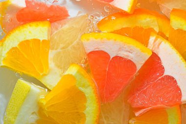 Pieces of grapefruit, orange fruit and honey pomelo in liquid with bubbles. Slices of  grapefruit, orange fruit and honey pomelo in water. Fresh slices of  grapefruit, orange fruit and honey pomelo on white background. Top view, flat design. Horizont