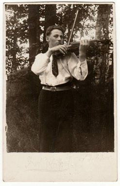The CZECHOSLOVAK REPUBLIC - 8 Mart 1923: Klasik fotoğraf genç adamın açık havada keman çaldığını gösteriyor. Antika siyah beyaz fotoğraf.