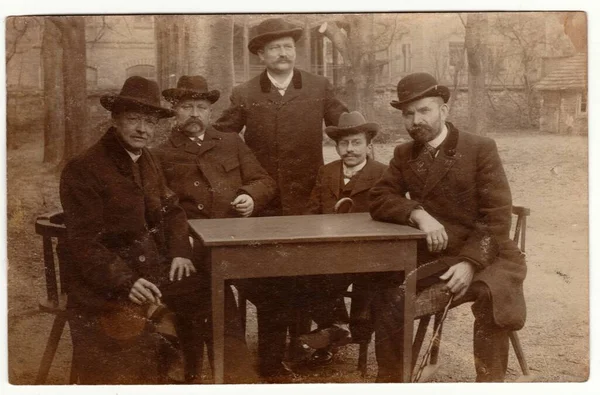 GERMANY - APRIL 14, 1907 Vintage photo shows men wear bowlers and sit at the table. Retro black and white photography. Circa 1900s.