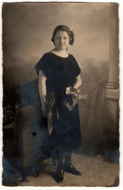 ALMANY - CIRCA 1920 'ler: Klasik fotoğraf kısa saçlı kadınları gösteriyor. Kadın siyah elbise giyiyor ve elinde buket çiçek tutuyor. Sepya efektli siyah beyaz stüdyo fotoğrafçılığı. Yaklaşık 1920 'lerde..