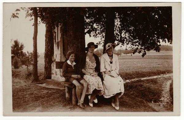 チェコスロバキア共和国 Circa 1930 ヴィンテージ写真は女性がエレガントなドレスと女性のパリソル大きなつばの帽子を身に着けていることを示しています 女と少年は屋外でポーズをとってベンチに座る レトロな黒と白の写真 1930年代 — ストック写真