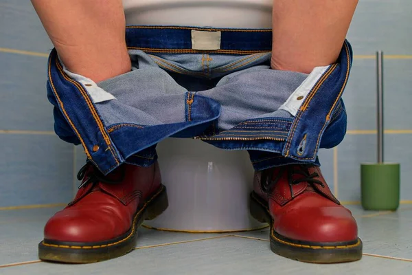 stock image A man sitting on the toilet. A concept from the 1980s. Red punk shoes and jeans. Gender theme and urban culture