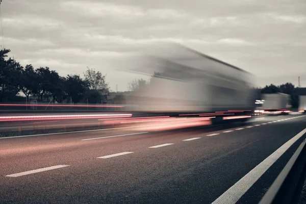 A truck driving on the highway at dusk. Motion blur on the highway. Evening shot of a truck. Concept of international transport and logistics. Almost monochrome image