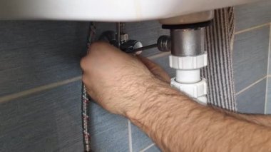 Tesisatçı musluktan lavaboya bağlantı çubuğunu tamir ediyor. Bir adamın elleri banyo musluğunun altındaki tesisatı tamir eder. Evdeki küçük onarımlar, oda servisi, DIY, bakım, el sanatları