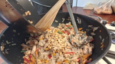 Şef tavuklu erişteye fındık serpiyor. Adamın elleri WOK tavasında dilimlenmiş tavuğa fıstık serpti. Gastronomi, aşçılık, ev yemeği kavramı. Bir adam yemek yapıyor..