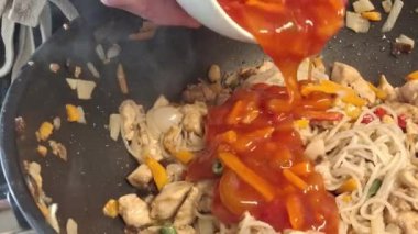 Aşçı WOK tavasındaki tavuklu erişteye acı sos ekler. Erkek elleri WOK tavasına kesilmiş tavuklu erişteye acı sos döker. Gastronomi, aşçılık, ev yemeği kavramı. Bir adam yemek yapıyor..