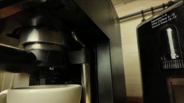 Kol kahve makinesinden kahve damlaları. Kahve makinesinden damlayan kahve damlaları. Arka planda espresso çekirdeği için elektrikli öğütücü var. Süper yavaş çekim.