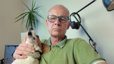 Bir usta av köpeğini okşar. Bir köpek ve efendisi oturma odasındaki kırmızı koltukta birlikte otururlar..