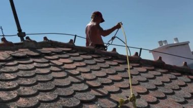 Çatı işçisi çatıyı koruyor. Çatı işçisi, emniyet ipi ve çatı emniyet seti. Çatı işçisi emniyet kemerini ayarlıyor. Yükseklerde çalışırken iş güvenliği kavramı.