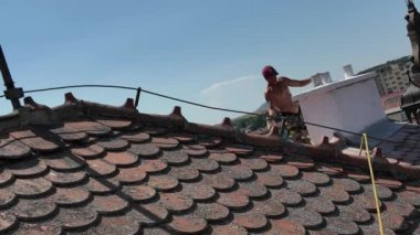 Bir işçi çatıda bir baca tamir eder. Bir işçi çatıyı tamir eder. Çatıda güvenlik ipi ve çatı emniyet kemeri olan bir işçi var. İnşaat işi ve yükseklerde çalışma kavramı.